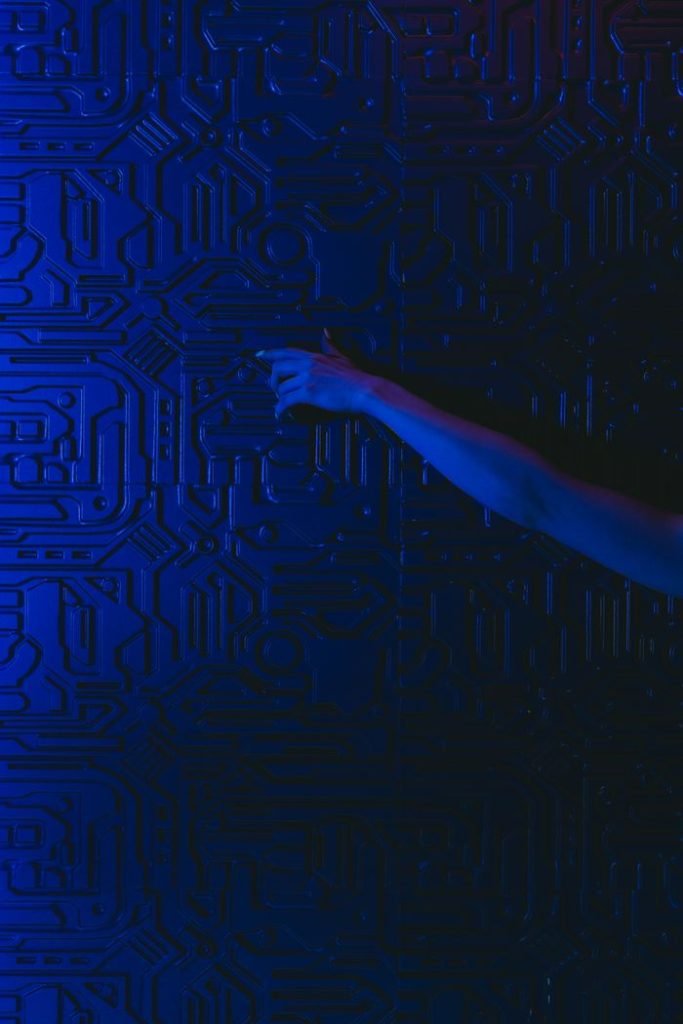 A hand reaches out to touch a futuristic blue circuit patterned wall with dramatic lighting.